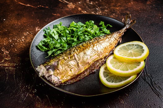 Grilled Mackerel Scomber fish on a plate with greens and lemon. Dark background. Top view photo