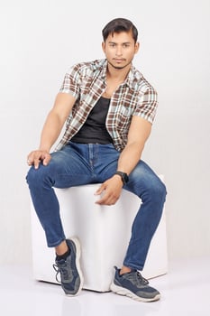 A man in jeans and a plaid shirt sitting on a white box photo