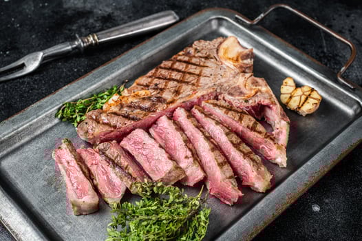 Medium rare Grilled T-Bone Steak, Florentine steak sliced in a steel tray. Black background. Top view photo