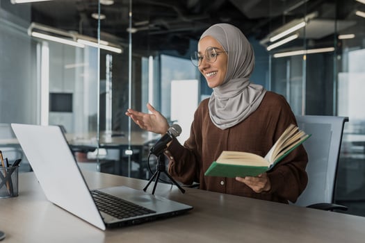 Young beautiful muslim woman in hijab working in modern office using professional microphone to record audio podcast reading religious book online radio photo