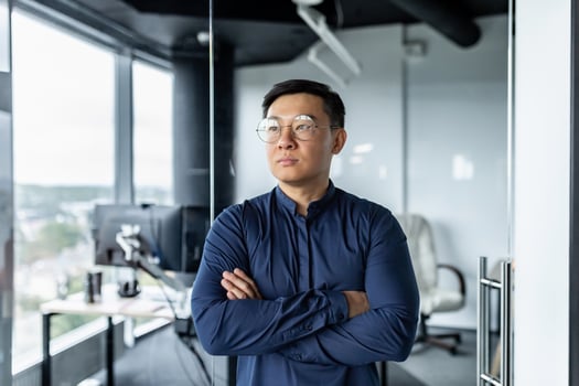 Thinking businessman with crossed arms in glasses looking out window, asian developer working inside modern office building. photo
