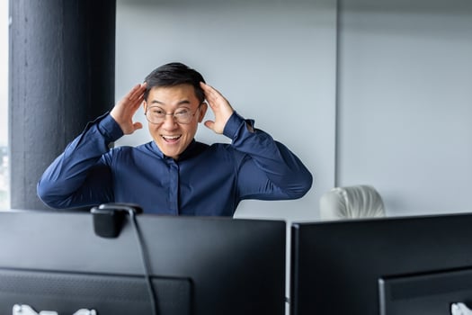 Happy business broker looking at two paired computer monitors and happy, businessman working inside modern office building, asian man celebrating successful deal and signed contract. photo