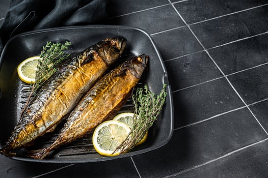 Grilled mackerel fish with lemon, herbs and spices in a skillet. Black background. Top view. Copy space photo