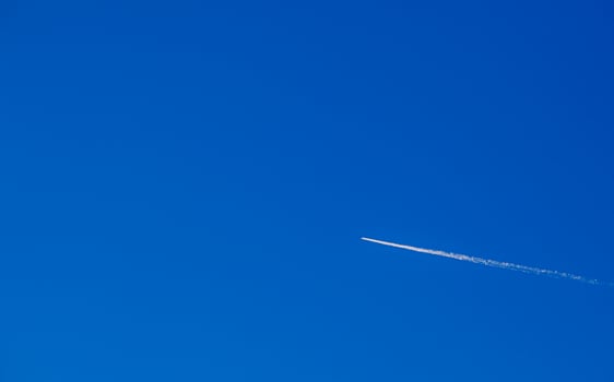 Flight of an airplane with a white trail diagonally against a clear blue sky. For text. photo