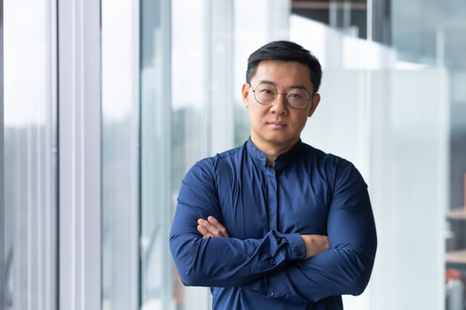 Portrait of asian businessman inside modern office, boss in glasses serious looking at camera, man with crossed arms thinking worker. photo