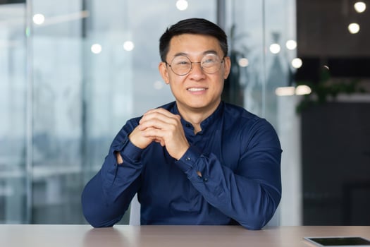 Young successful Asian businessman looking at caper and smiling, call sitting at table investor boss in shirt and glasses. photo