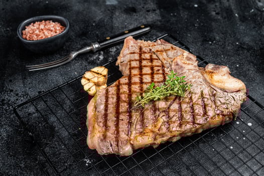Grilled T-bone or Porterhouse beef meat Steak on a rack. Black background. Top view photo