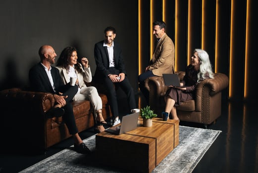 Five professionals engage in a lively discussion in a stylish office space. They share ideas on business strategies while sitting on cozy sofas around a wooden coffee table. photo