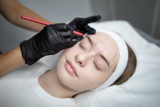 A beauty technician carefully applies a makeup procedure on a client's eyebrows at a salon. The client relaxes with closed eyes as the artist focuses on creating a long-lasting effect. photo