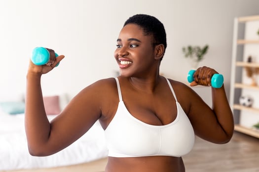Plus size young black lady exercising with dumbbells at home during covid lockdown, banner design. Happy overweight Afro woman strengthening arm muscles, having weight loss training indoors photo