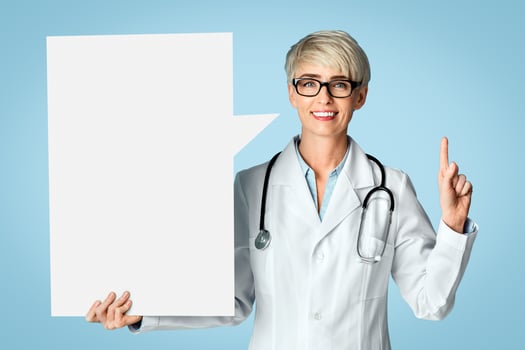 Doctor recommendations. Woman therapist points finger up and holds abstract empty space for words, isolated on blue background, studio shot photo