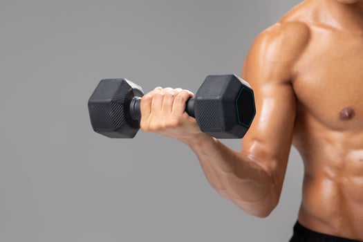 A young Brazilian man with an athletic build engages in strength training by lifting a dumbbell. He is focused on maintaining a healthy lifestyle while exercising indoors against a plain background. photo