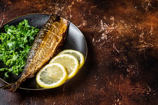 Grilled Mackerel Scomber fish on a plate with greens and lemon. Dark background. Top view. Copy space photo