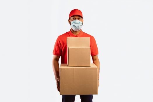 Quarantine Delivery Service. African American Courier Holding Boxes Delivering Items Purchased Online Posing On Yellow Studio Background Wearing Protective Mask. photo