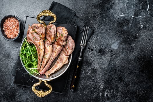 Grilled Lamb mutton Chops steaks in a skillet with green salad. Black background. Top view. Copy space photo