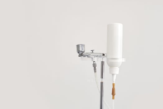 Airbrush makeup system with white bottle and metal components on stand. photo