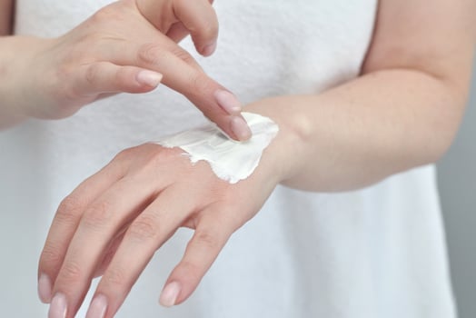 Female applying moisturizing cream on hand for skincare routine with caucasian adult hands. photo