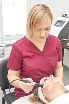 Female caucasian adult aesthetician performing facial treatment on female client with modern equipment in spa clinic. photo