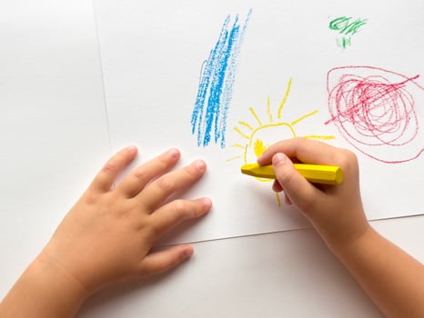 Childs hand drawing colorful crayon sun on white paper photo