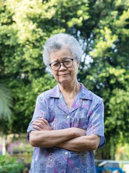 Portrait of a senior woman with short gray hair looking at the camera with a smile while standing arms crossed in the garden photo