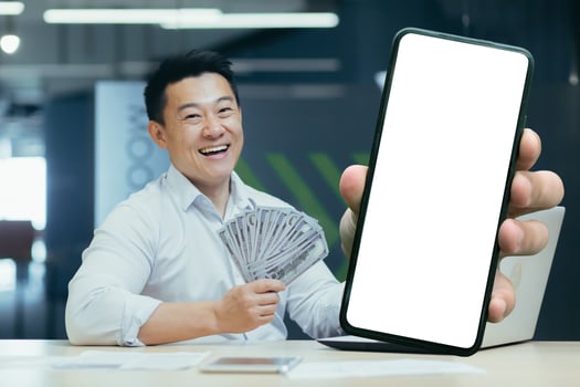 Asian happy businessman in office, showing phone screen with white phone, and holding dollar cash in hands, boss director happy with received loan photo