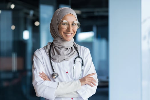 Portrait of Arabic female doctor in modern clinic, Muslim woman wearing hijab glasses and white medical coat working in hospital office, smiling and looking at camera with crossed arms photo