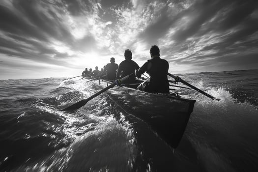 A black and white image of a rowing crew powerfully navigating choppy ocean waves towards a dramatic, sunlit sky photo