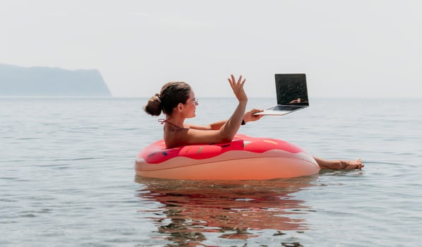 Woman Laptop Beach - Working remotely on vacation while floating on an inflatable ring in the ocean. photo