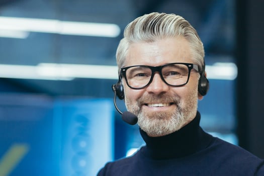 Portrait of a gray-haired handsome man in glasses and a headset with a microphone. Speaker, business trainer, online conference. Looking at the camera, smiling. photo