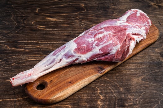 Mutton meat. Raw whole lamb leg thigh on butcher board. Wooden background. Top view photo