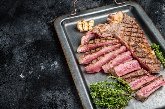 Medium rare Grilled T-Bone Steak, Florentine steak sliced in a steel tray. Black background. Top view. Copy space photo