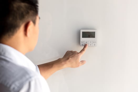 Close-up photo. The finger of a man's hand in a white shirt includes the buttons of the control panel of the air conditioner on the wall of the house, office. photo