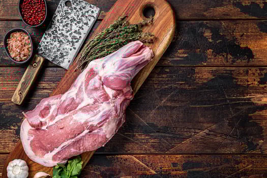 Raw lamb whole shoulder, fresh leg meat on a wooden board with spices. Wooden background. Top view. Copy space photo