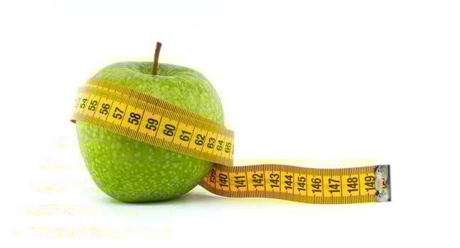 Green Apple Wrapped With a Yellow Tape Measure on White Background photo