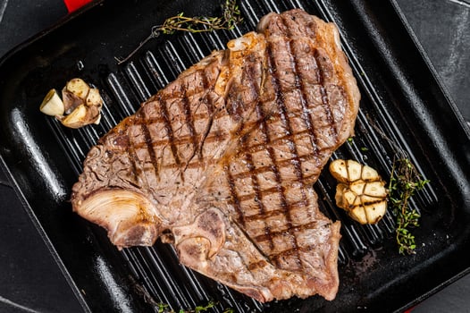 Grilled T-bone, t bone beef meat Steak on a grill skillet. Black background. Top view photo