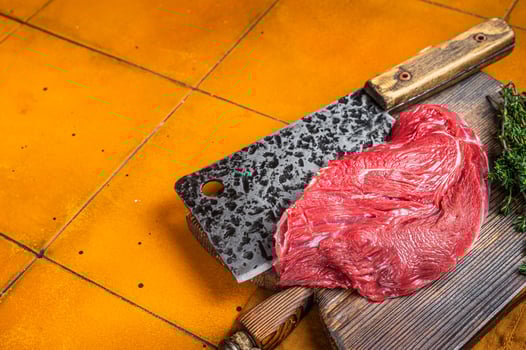 Piece of Raw beef meat for stew with herbs on butcher cutting board. Orange background. Top view. Copy space photo