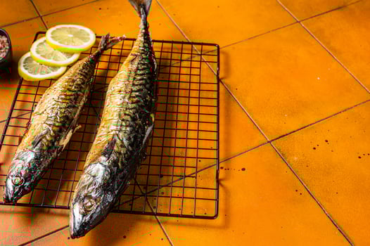 Roast Mackerel Scomber fish with lemon, herbs and spices on a grill. Orange background. Top view. Copy space photo