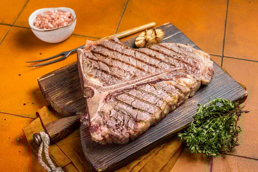 BBQ Roast T bone or Porterhouse beef meat Steak on a wooden board with spices. Orange background. Top view photo