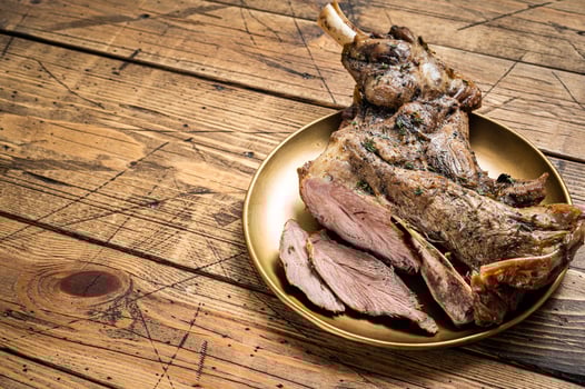 Baked whole lamb shoulder leg with herbs and spices in a steel plate. Wooden background. Top view. Copy space photo