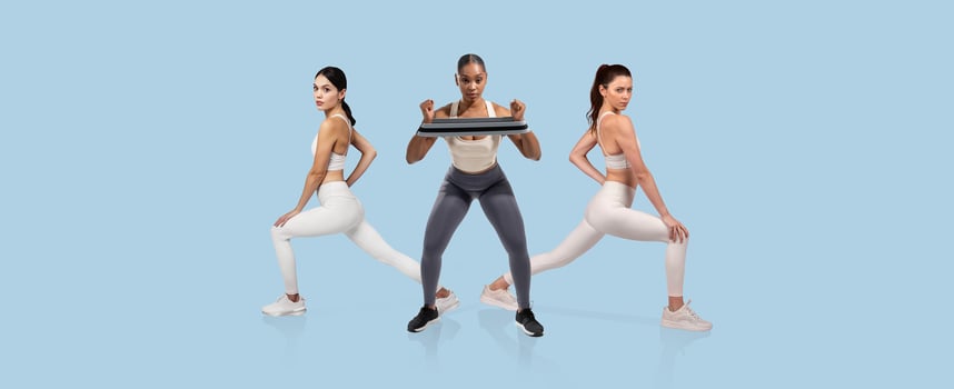 Three women are actively engaged in a workout, performing lunges and lifting weights in a bright, spacious fitness studio. The atmosphere is focused and energetic. photo