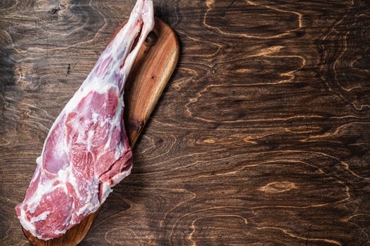Mutton meat. Raw whole lamb leg thigh on butcher board. Wooden background. Top view. Copy space photo