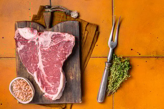 Porterhouse raw beef meat Steak, T-bone with thyme and sea salt on a wooden board. Orange background. Top view photo