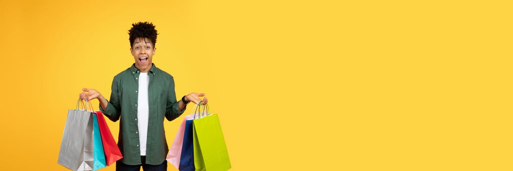 Surprised and happy young black man holding several shopping bags with a cheerful look, copy space photo