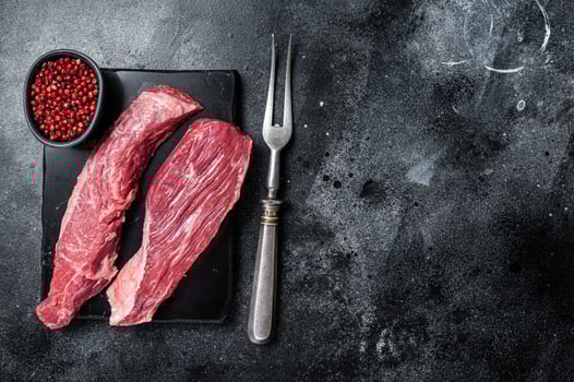 Bavette raw beef meat steak or Sirloin flap on marble board. Black background. Top view. Copy space photo