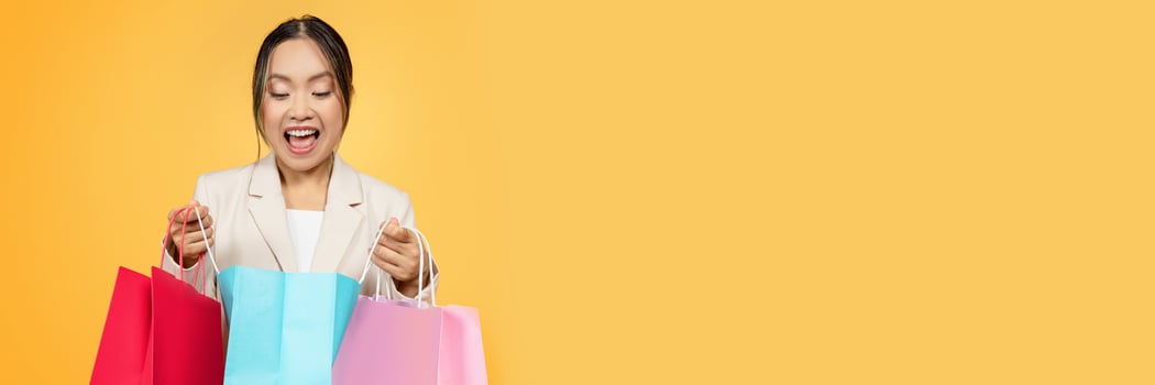 Surprised glad young korean lady shopaholic open colorful bags, with purchases enjoy shopping, isolated on orange studio background. Huge sale, fashion, present and new purchases, copy space photo