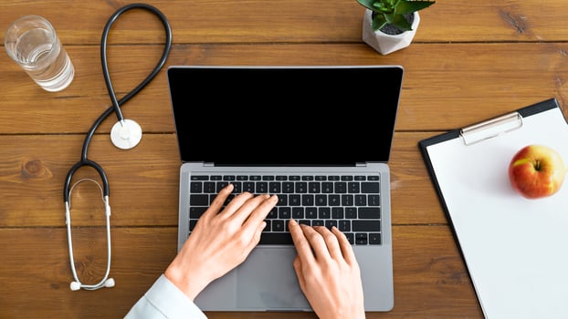 Blog and online doctor consultation.Female hands in white coat on laptop with blank screen, near stethoscope, glass of water and tablet photo