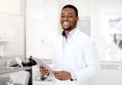Dentistry Services. Portrait of handsome black male dentist with digital tablet in hands posing in modern dental clinic interior, professional african american stomatologist doctor smiling at camera photo