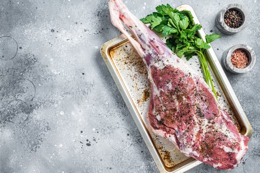 Marinated whole mutton leg, raw lamb meat with thyme, spices and olive oil. Gray background. Top view. Copy space photo