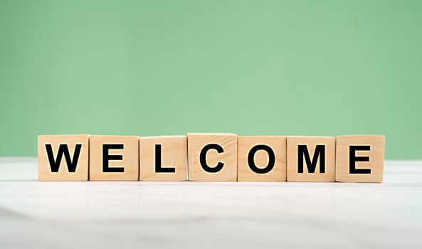Welcome word is written on wooden cubes on a marble floor with a green background photo