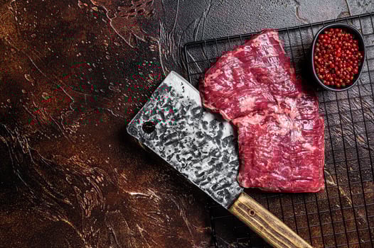 Raw skirt beef steak on meat cleaver. Black background. Top view. Copy space photo